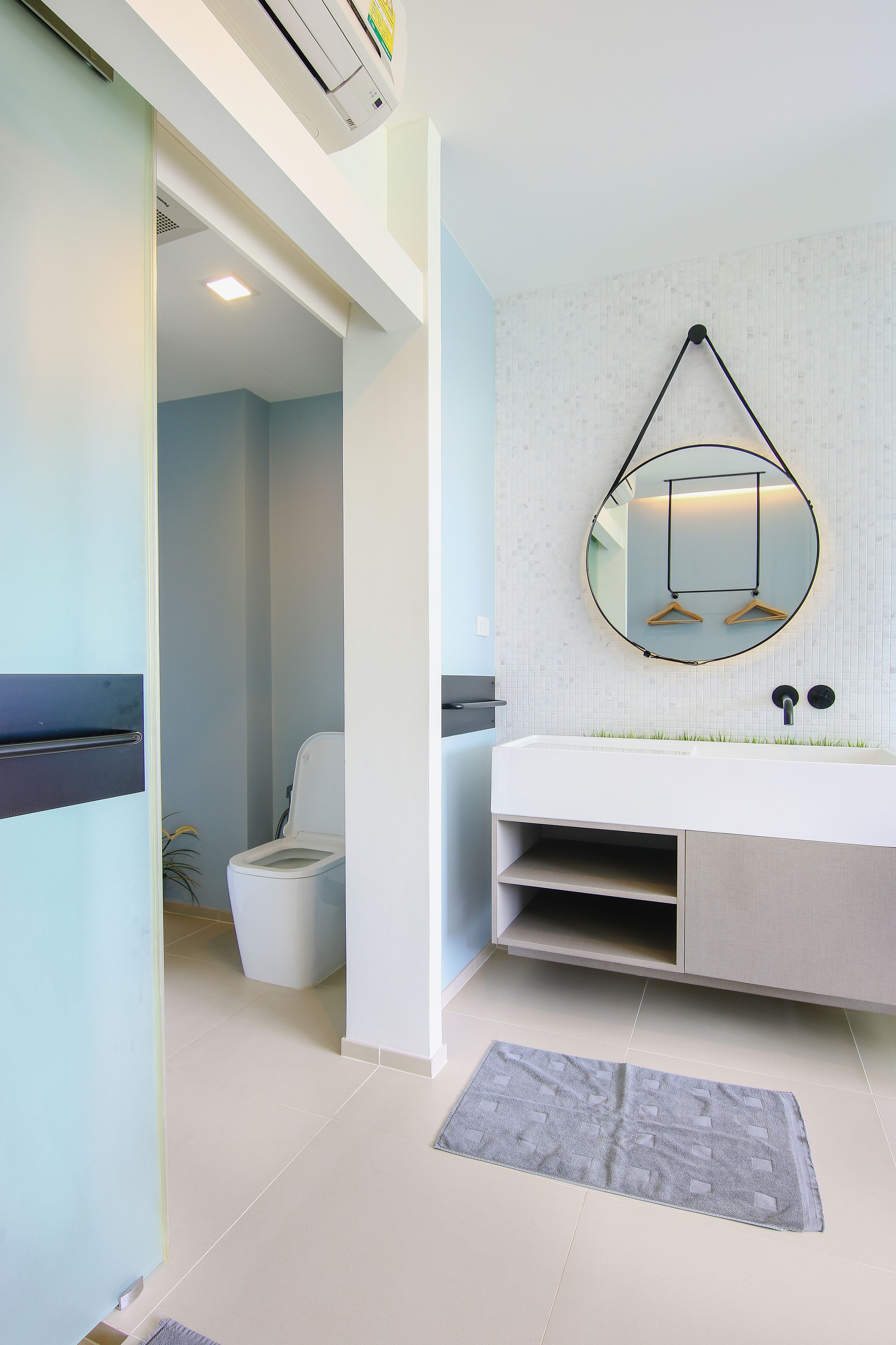 A modern bathroom with a white sink, a round mirror, and a towel rack.