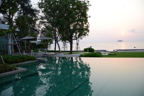 A serene pool area with a view of the sea and a distant island, surrounded by trees and outdoor furniture. - Hua Hin Luxury Beachfront Condo By Mon (Hua Hin)