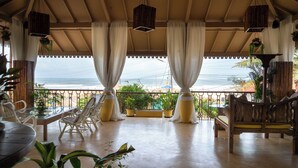 A covered outdoor seating area with a view of the ocean, featuring wicker chairs, a table, and potted plants. - Fiesta Beach Resort (Baga)