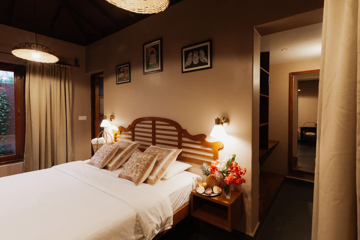Cama bem arrumada com almofadas, mesa de cabeceira com abajur e parede com quadros.