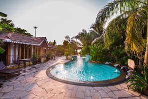 A pool area with a curved design, surrounded by stone flooring, lounge chairs, and potted plants. - Fiesta Beach Resort (Baga)