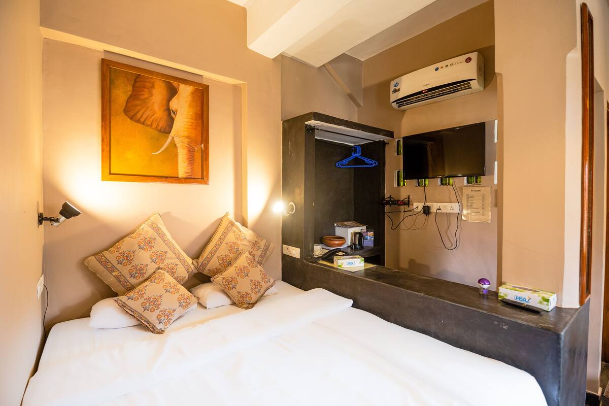 Quarto de hotel com cama, pintura de elefante, ar condicionado, espelho e televisão.