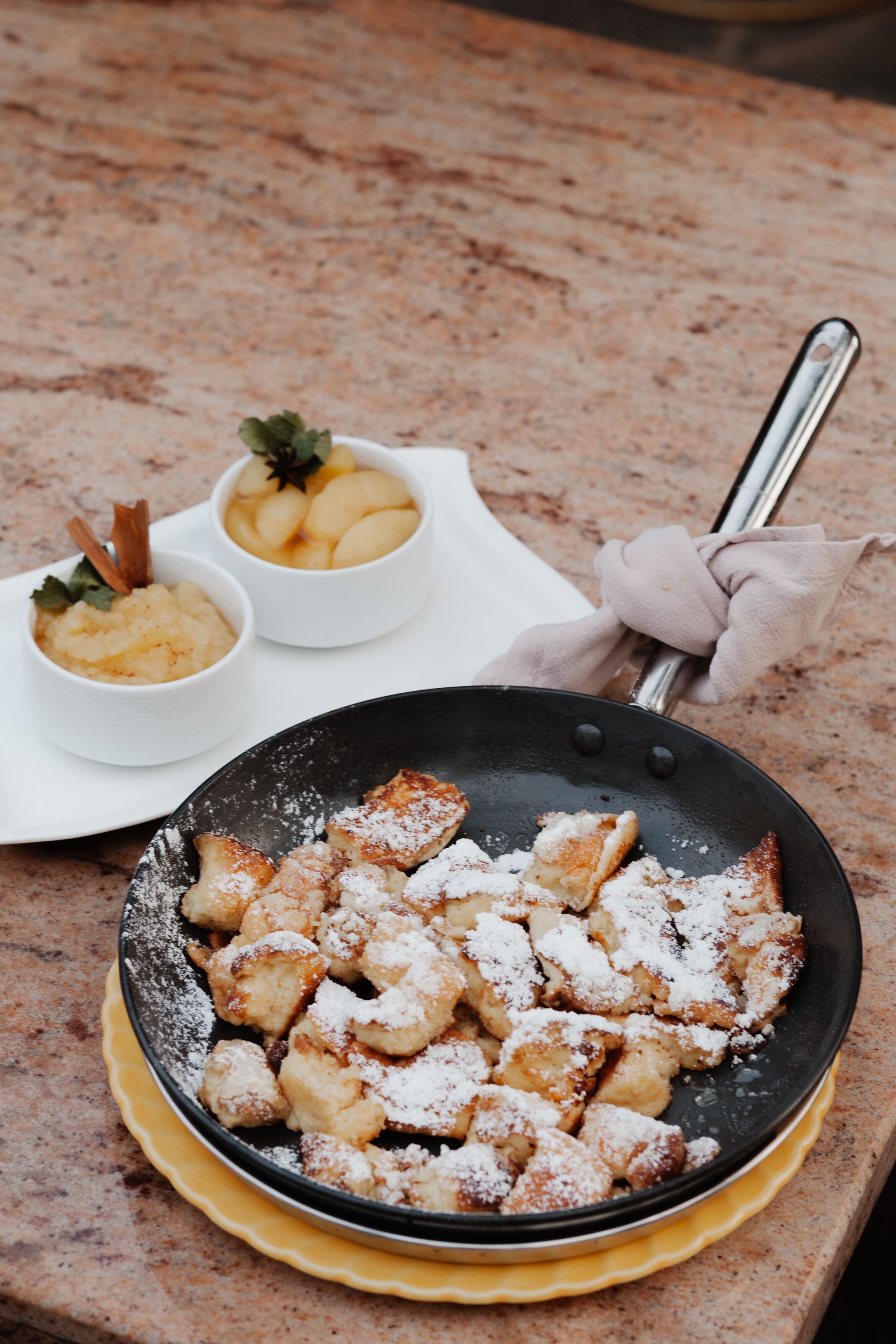 Eine Bratpfanne mit gebratenem Essen und zwei kleine Dessertschalen auf einer Marmorarbeitsplatte.