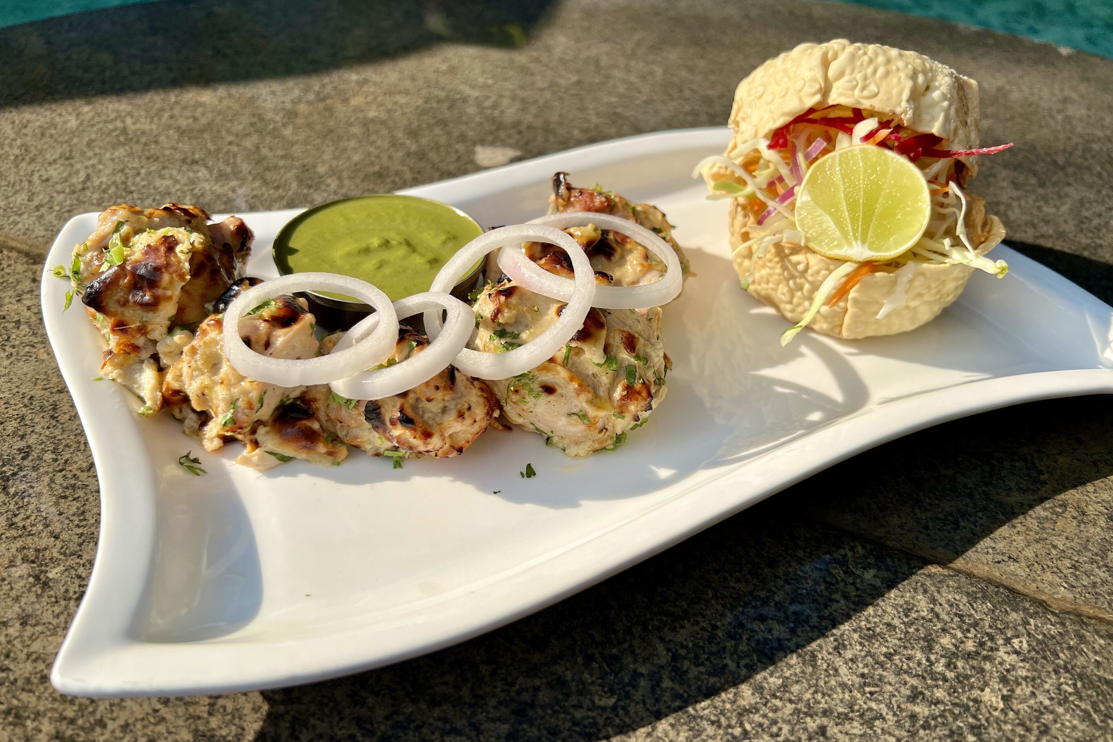 A white plate with grilled chicken skewers, a lime wedge, and a sandwich.