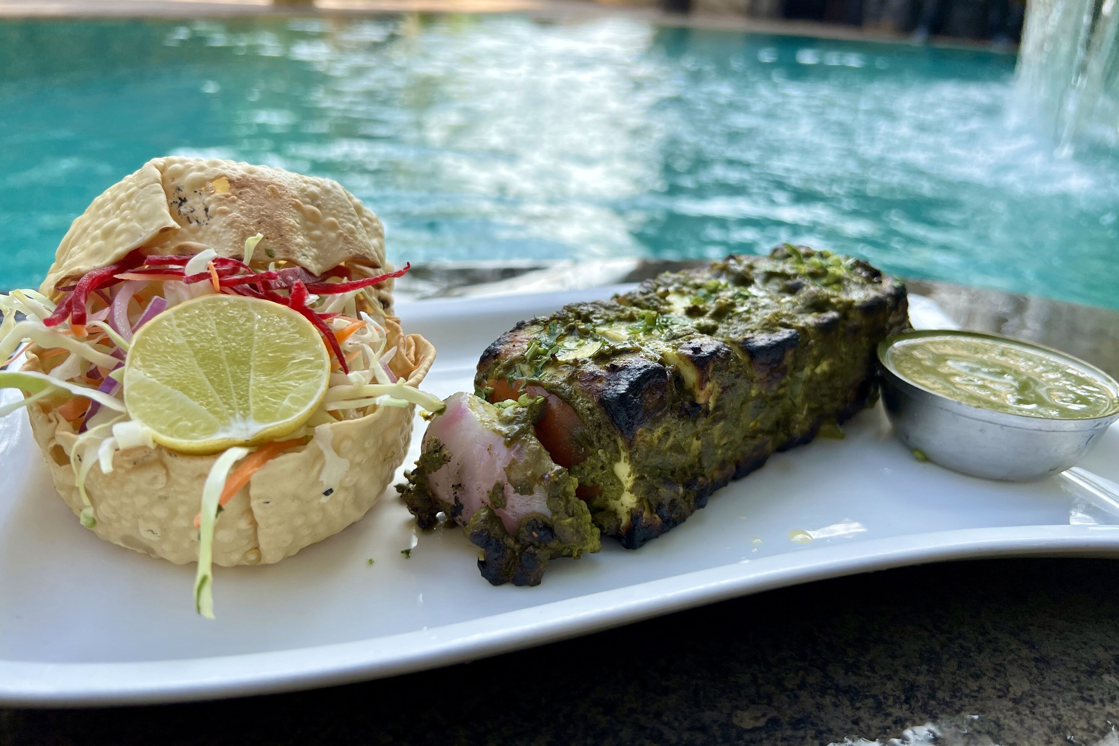 Ein Teller mit gegrilltem Fleisch, einem Wrap und einem gemischten Salat, im Hintergrund ist ein Pool zu sehen.