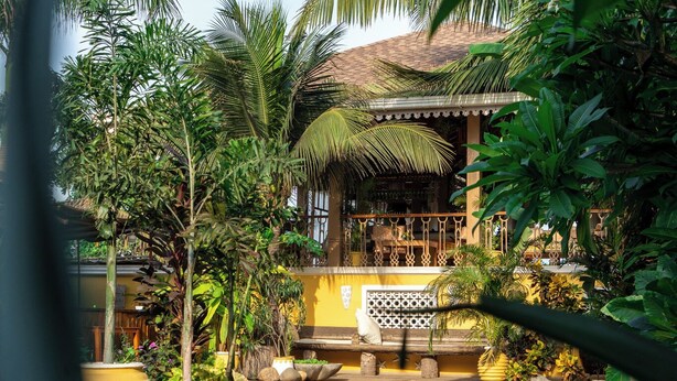 A pool area with a tropical setting, including palm trees and a building with a thatched roof. - Fiesta Beach Resort (Baga)