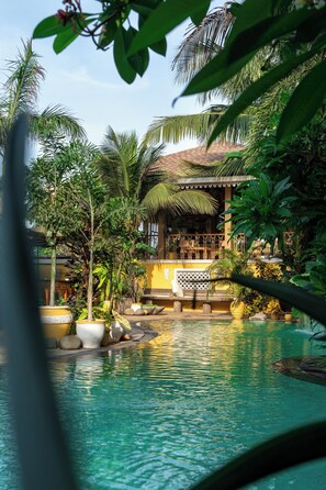 Un espace piscine aménagé dans un décor tropical, avec des palmiers et un bâtiment doté d’un toit de chaume.