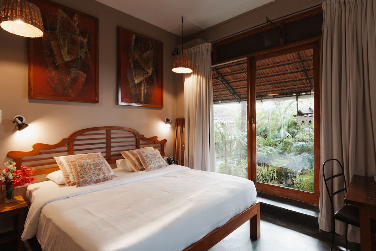 Quarto com cama grande, cabeceira de madeira e vista para um jardim através de uma porta de correr de vidro.