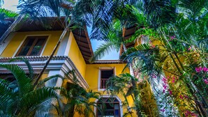 A yellow building with a balcony, surrounded by lush tropical plants and flowers. - Fiesta Beach Resort (Baga)