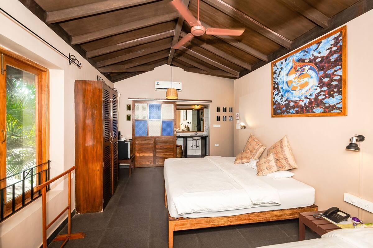 Quarto com cama de madeira, ventoinha no teto, um quadro e vista para o banheiro.