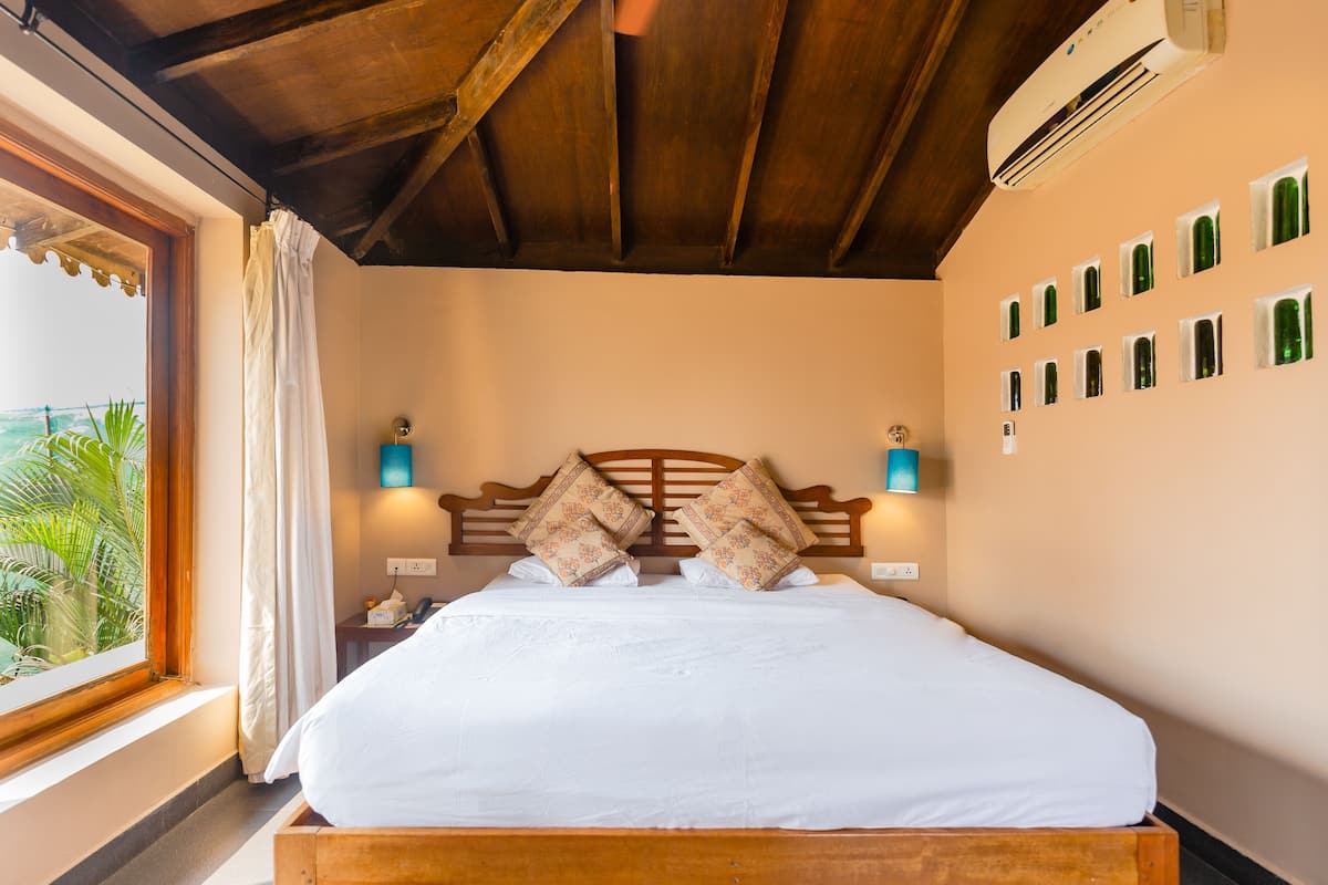 Quarto com cama de madeira, duas luminárias de cabeceira, janela com cortinas e parede com várias janelas pequenas.