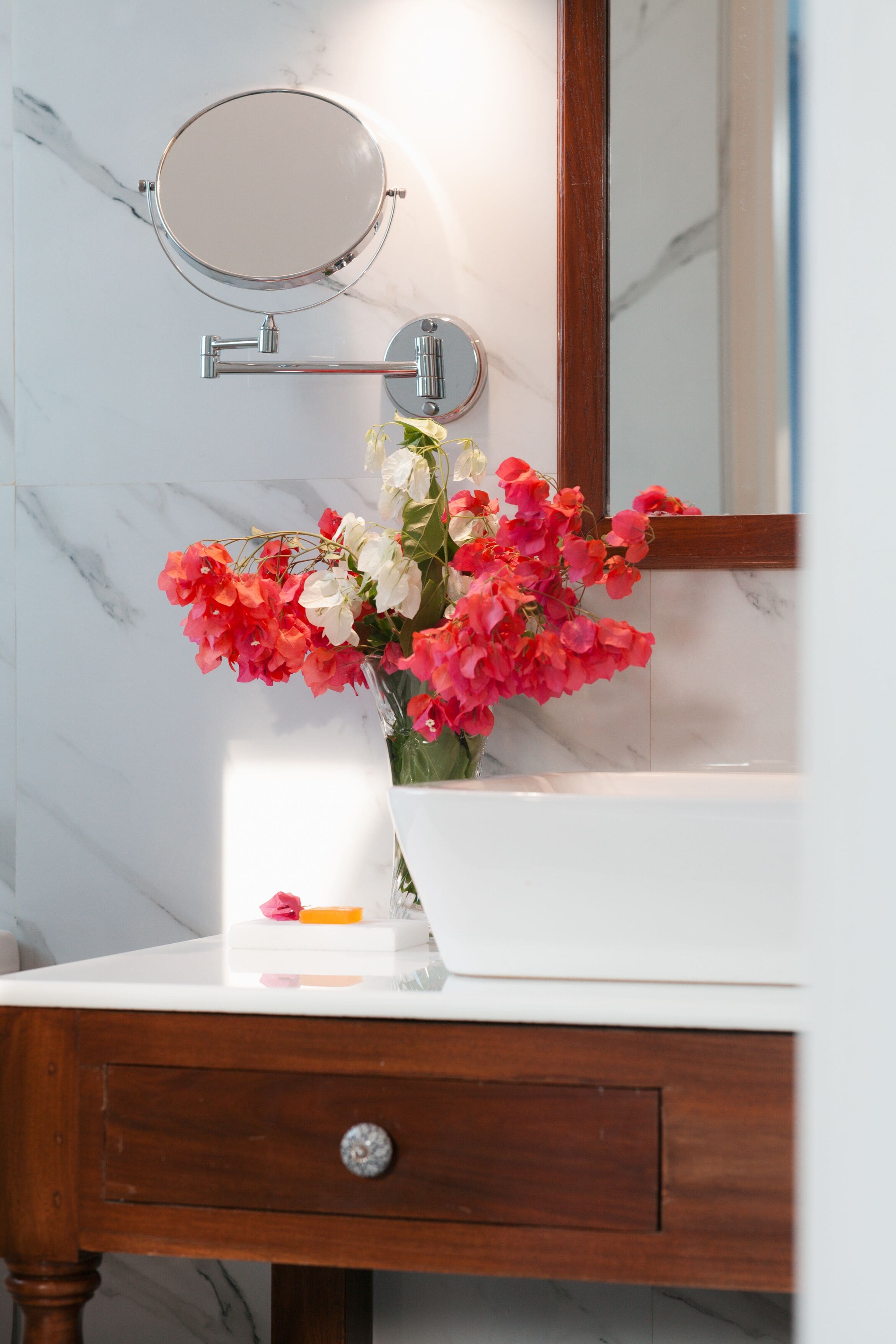 Un tocador de baño con encimera de mármol, un espejo y un florero con flores.