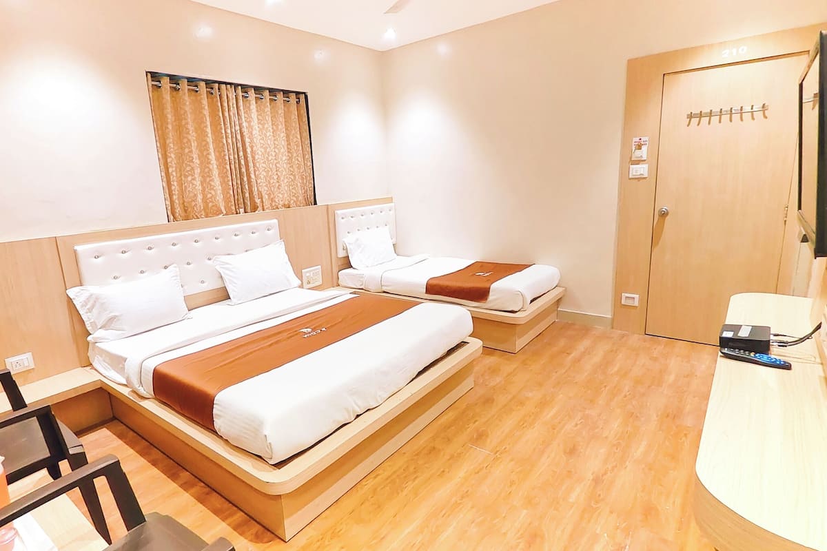 A hotel room with two beds, a desk, a chair, a TV, and a door with a number.