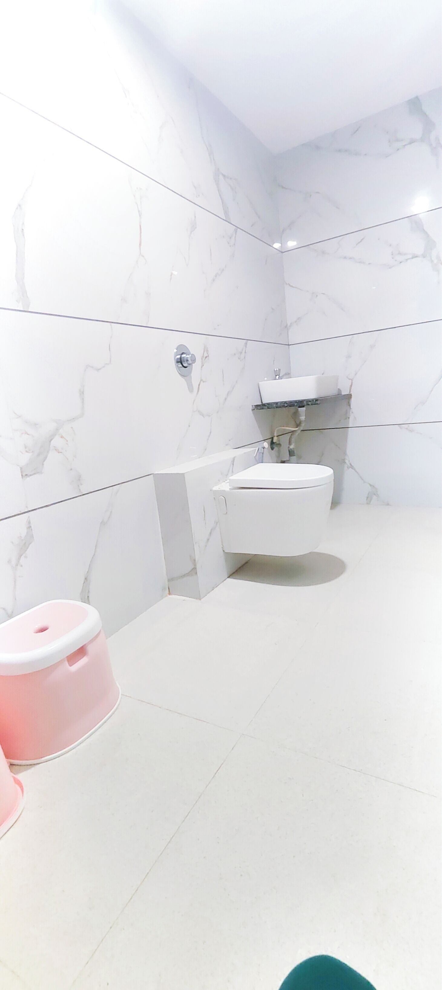 A bathroom with white marble walls and a white toilet.