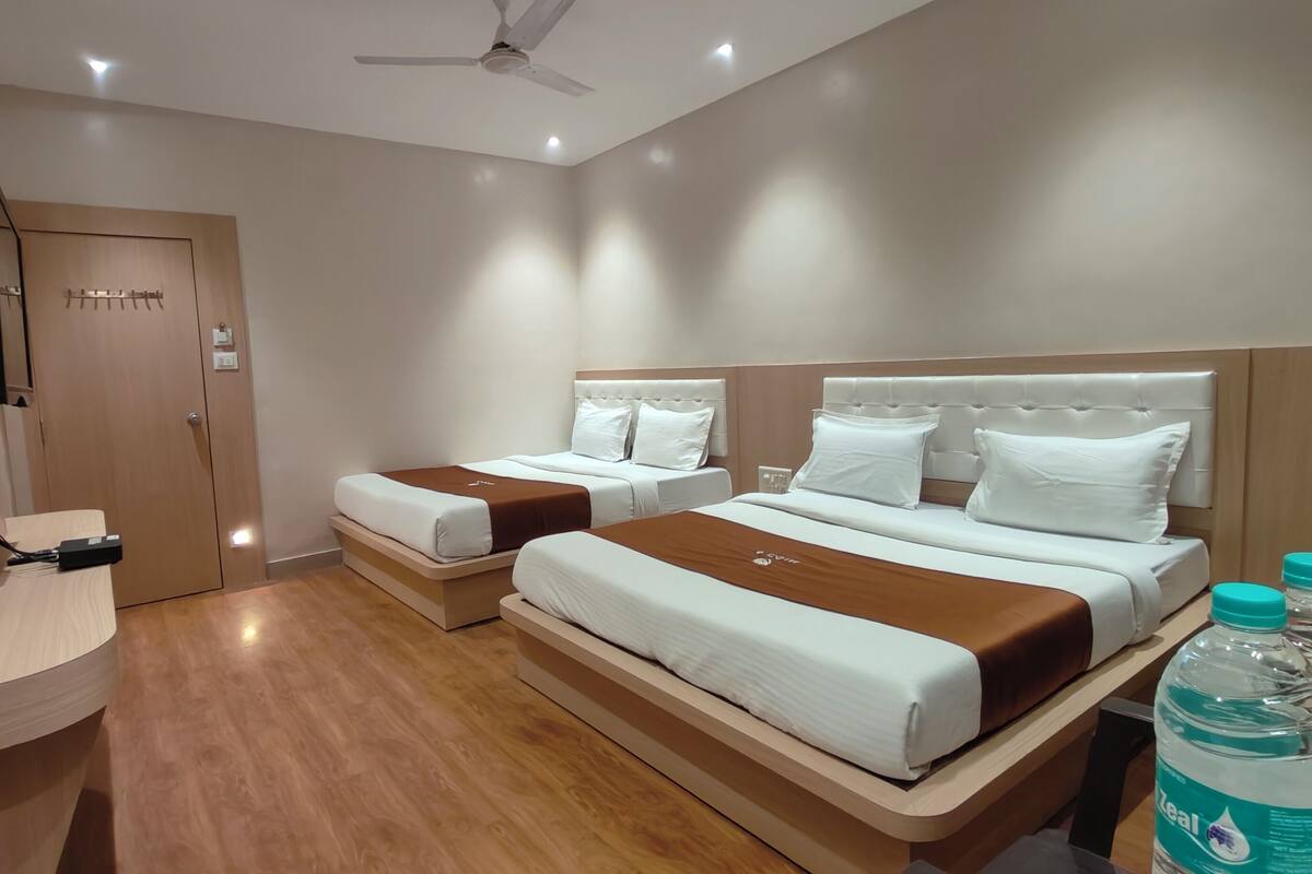 A hotel room with two beds, a flat-screen TV mounted on the wall, a ceiling fan, and a wooden floor.
