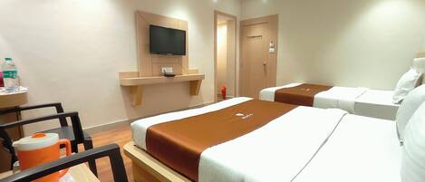 A hotel room with two beds, a TV mounted on the wall, a small table with a water bottle, and a chair.