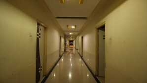 A long, narrow hotel corridor with doors on both sides, a tiled floor, and recessed lighting on the ceiling. - Hotel Yog Palace (Rahata)