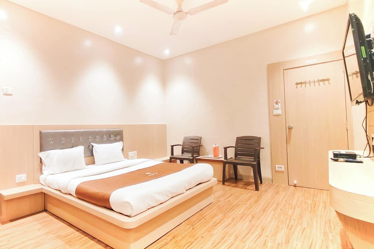 A hotel room with a large bed, a desk, two chairs, a ceiling fan, and a door with a number.