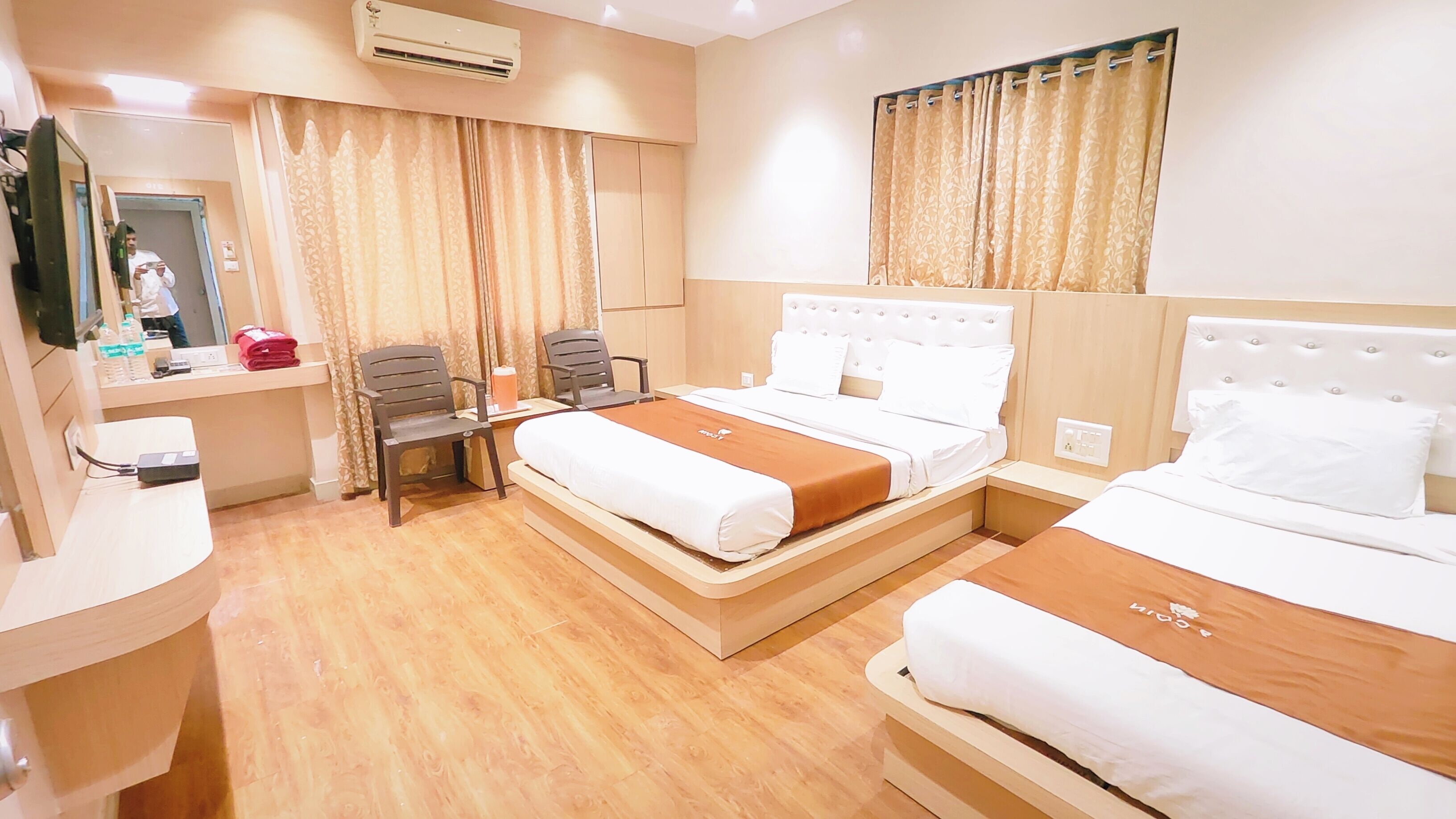 Quarto de hotel com duas camas, uma escrivaninha com cadeira, um espelho e um aparelho de ar condicionado.