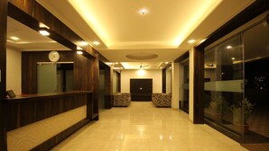 A hotel lobby with a reception desk, patterned seating, a clock, and a ceiling fan. - Hotel Yog Palace (Rahata)