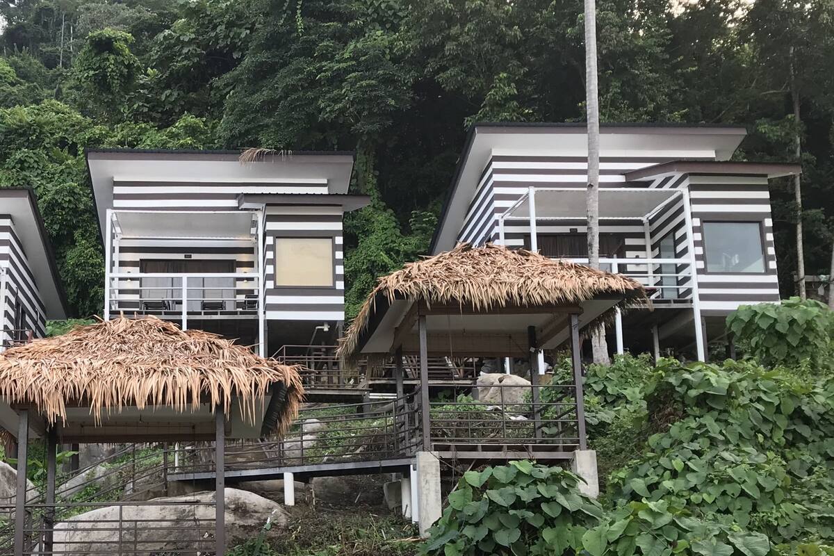 Tres edificios modernos de varios pisos con estructuras de techo de paja, rodeados de abundante vegetación.