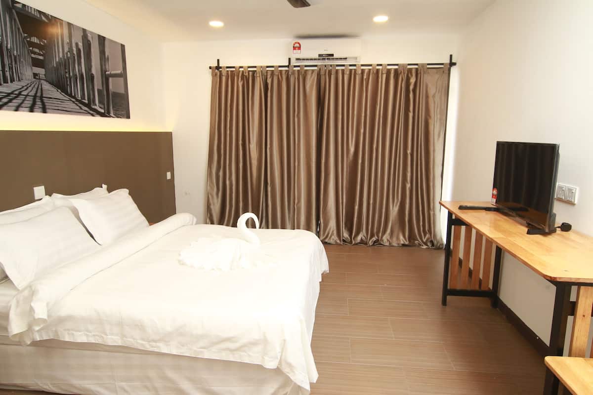 Habitación de hotel con cama, escritorio, televisor y cortina.