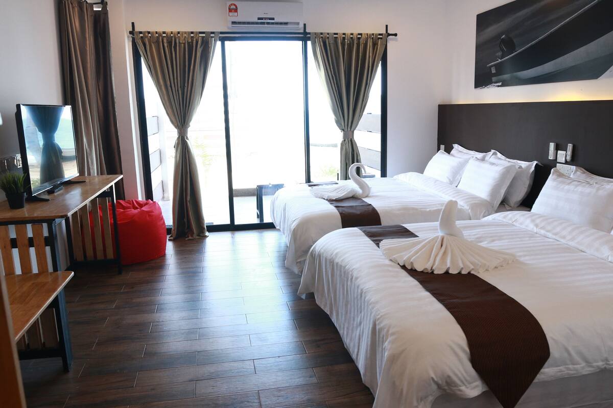 Habitación de hotel con dos camas, un televisor, un escritorio y un sillón de peluche rojo.