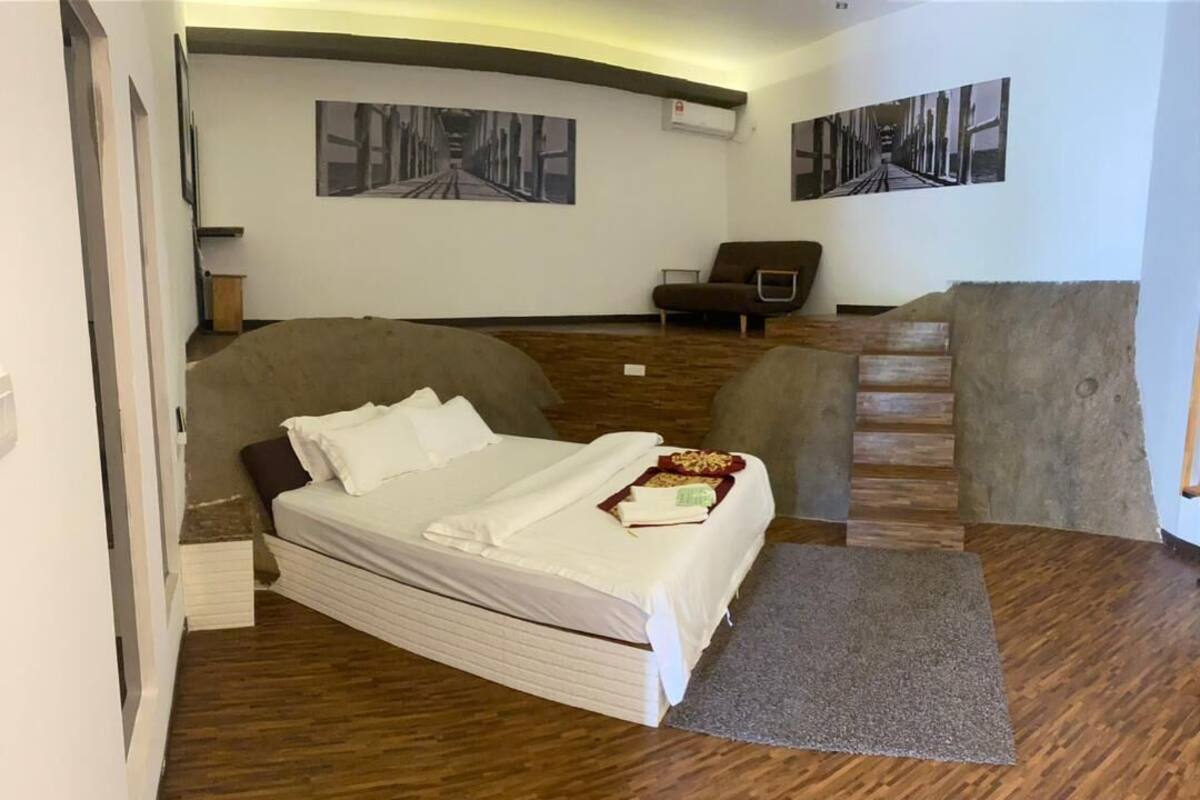 Un dormitorio con cama, una silla y una mesita. Hay dos cuadros en la pared.