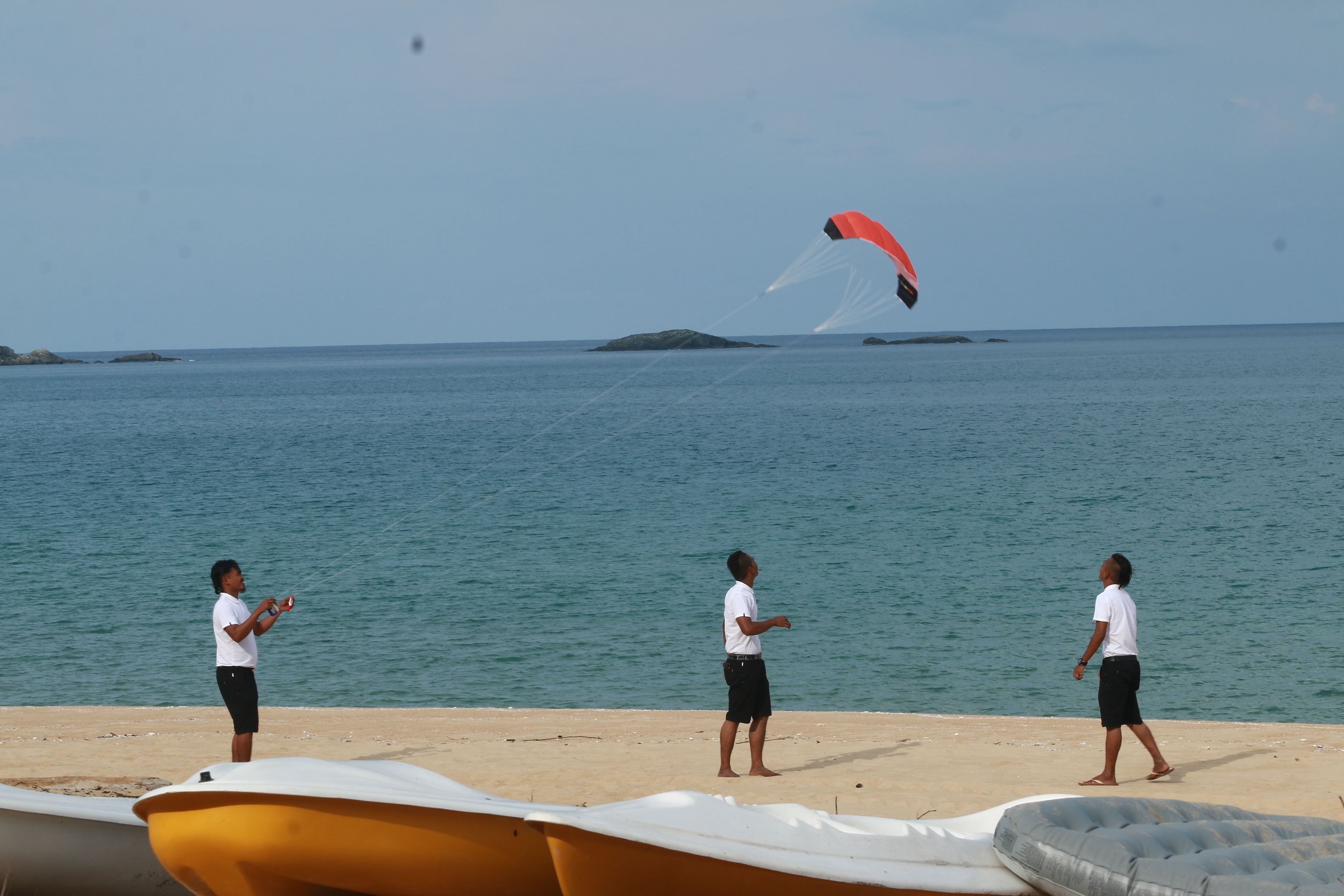 A beach with three people and a kite flying over the water.