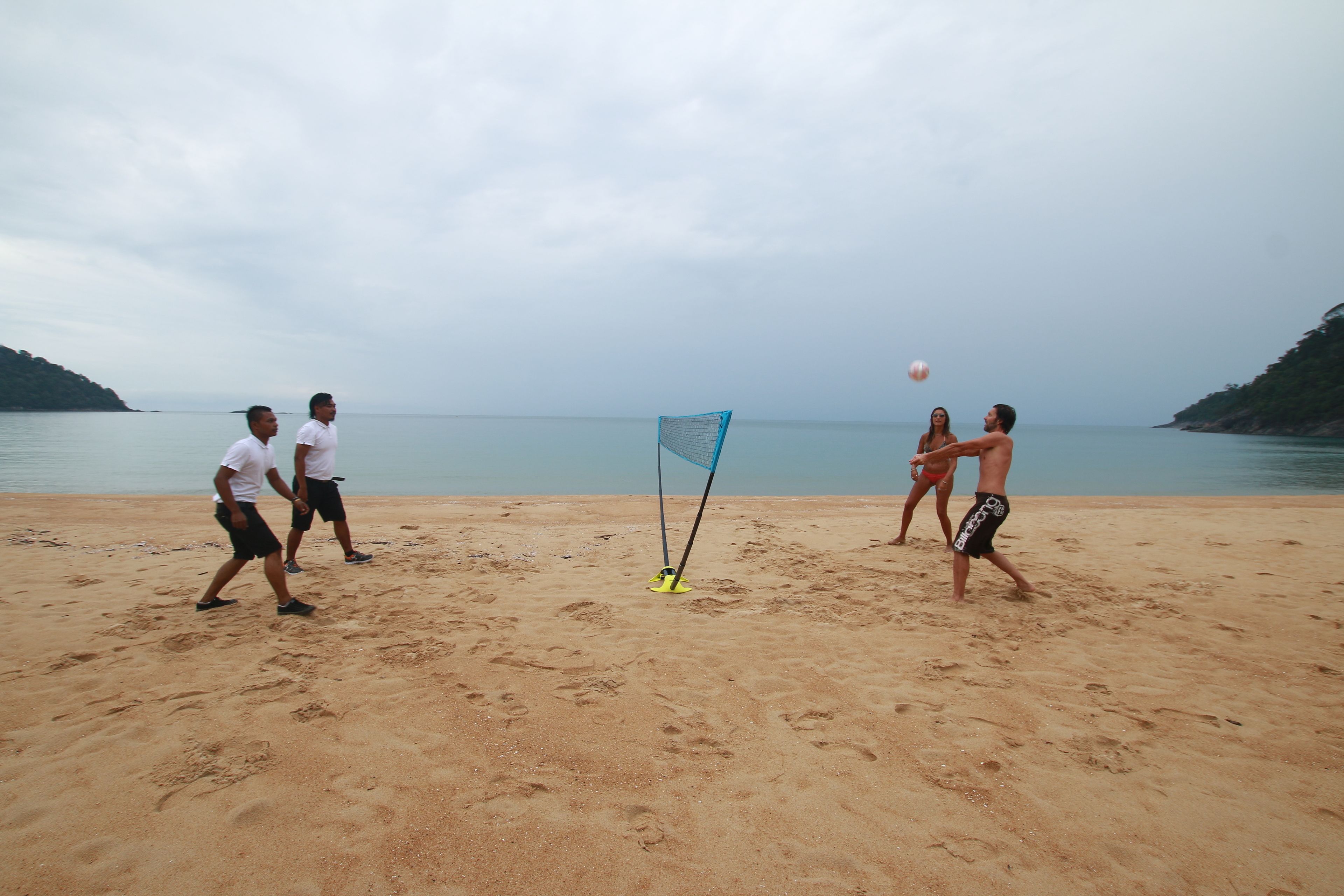 Partido de voleibol de playa con jugadores y una red sobre una playa arenosa.