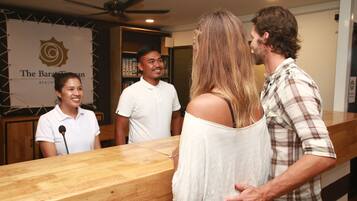 A reception area with a wooden counter, a sign reading "The Bar at The Baratan Beach," and a ceiling fan.