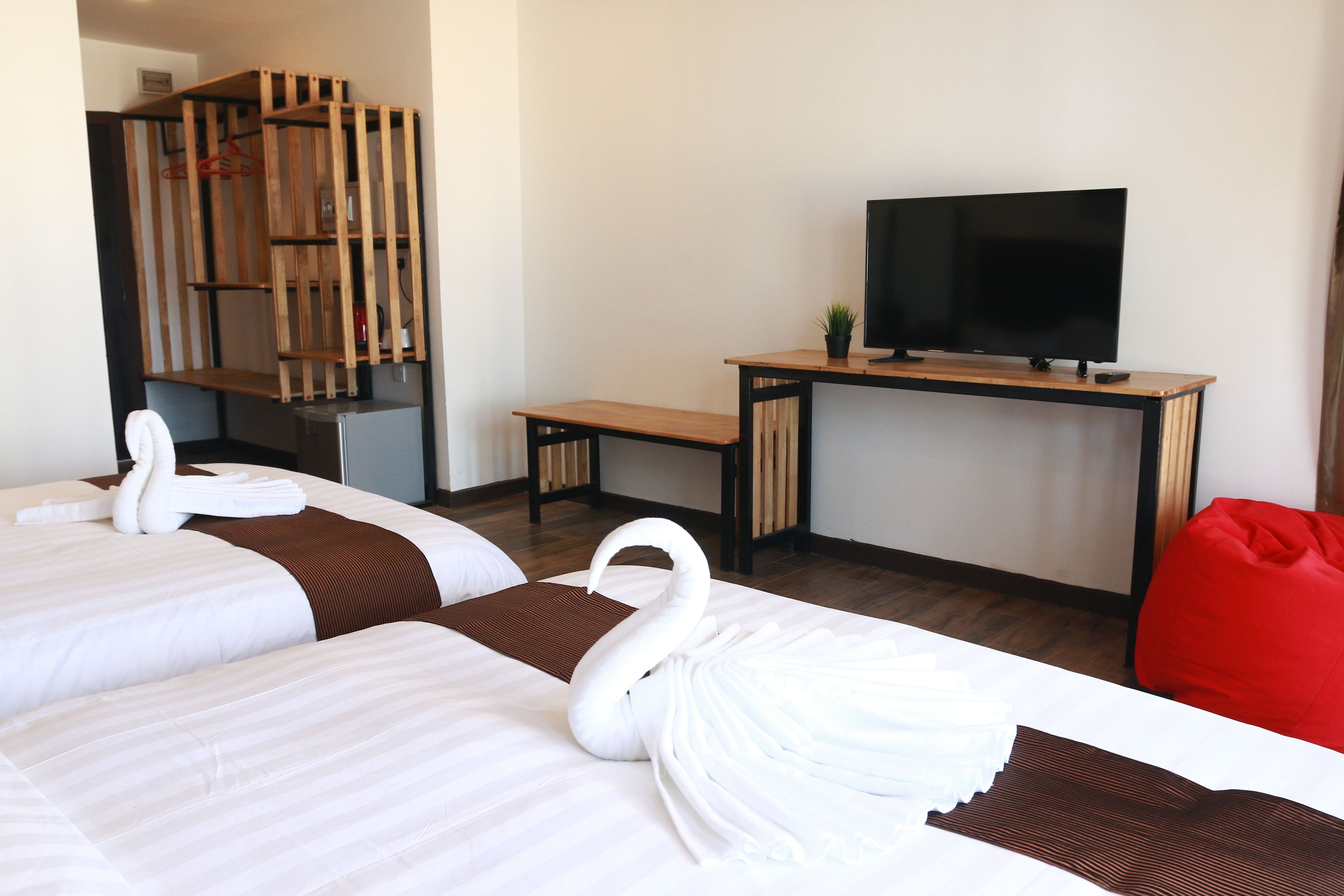 A hotel room with two beds, a wooden desk, a television, and a red bean bag.