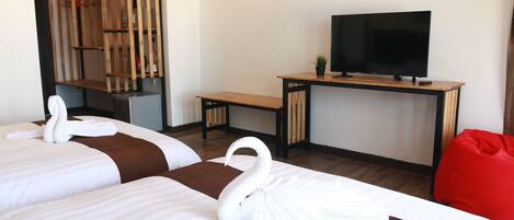 A hotel room with two beds, a wooden desk, a television, and a red bean bag.