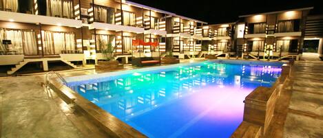 Un hotel con piscina, varios balcones y zonas de estar al aire libre.