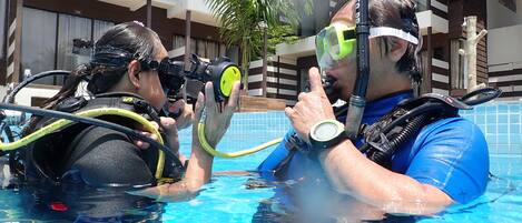 Dos personas en una piscina con equipo de buceo y sosteniendo cámaras.