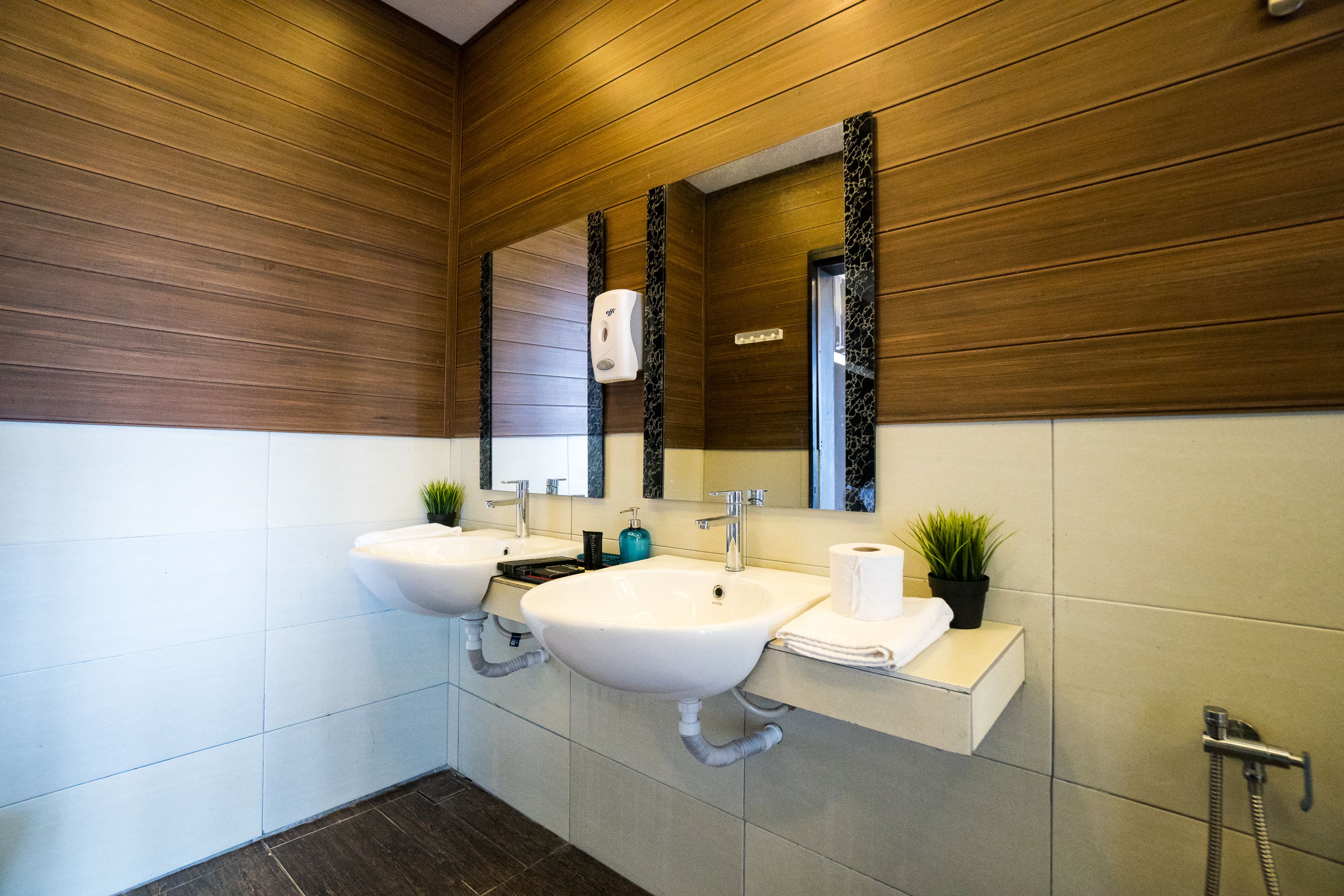 Un baño moderno con dos lavamanos, un espejo, dispensador de jabón y perchero para toallas.