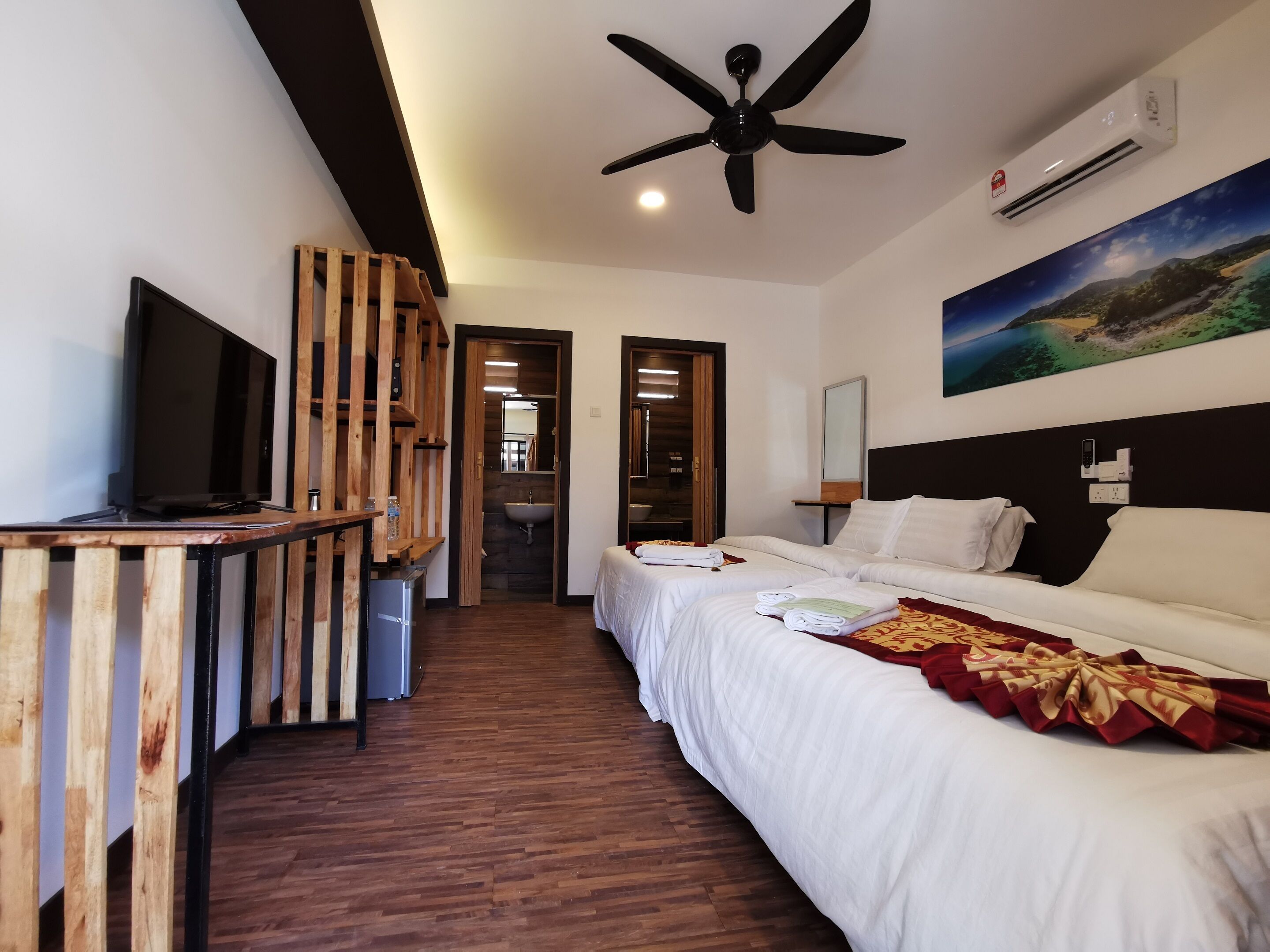 A hotel room with a bed, a TV, a ceiling fan, an air conditioner, and a painting on the wall.