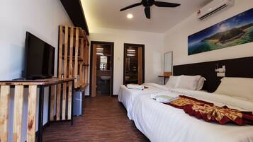 A hotel room with a bed, a TV, a ceiling fan, an air conditioner, and a painting on the wall.