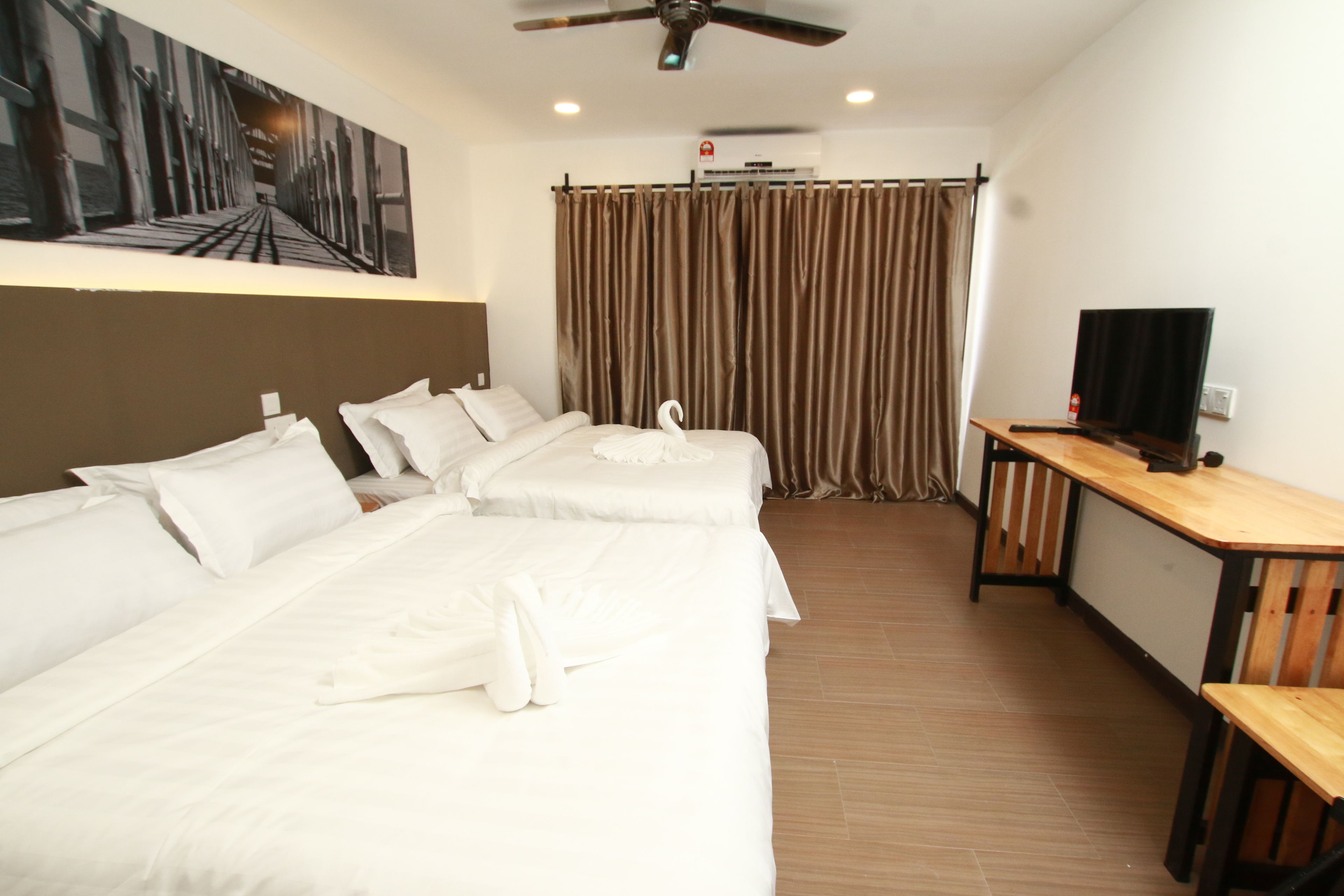 A hotel room with two beds, a TV, a ceiling fan, and a painting on the wall.