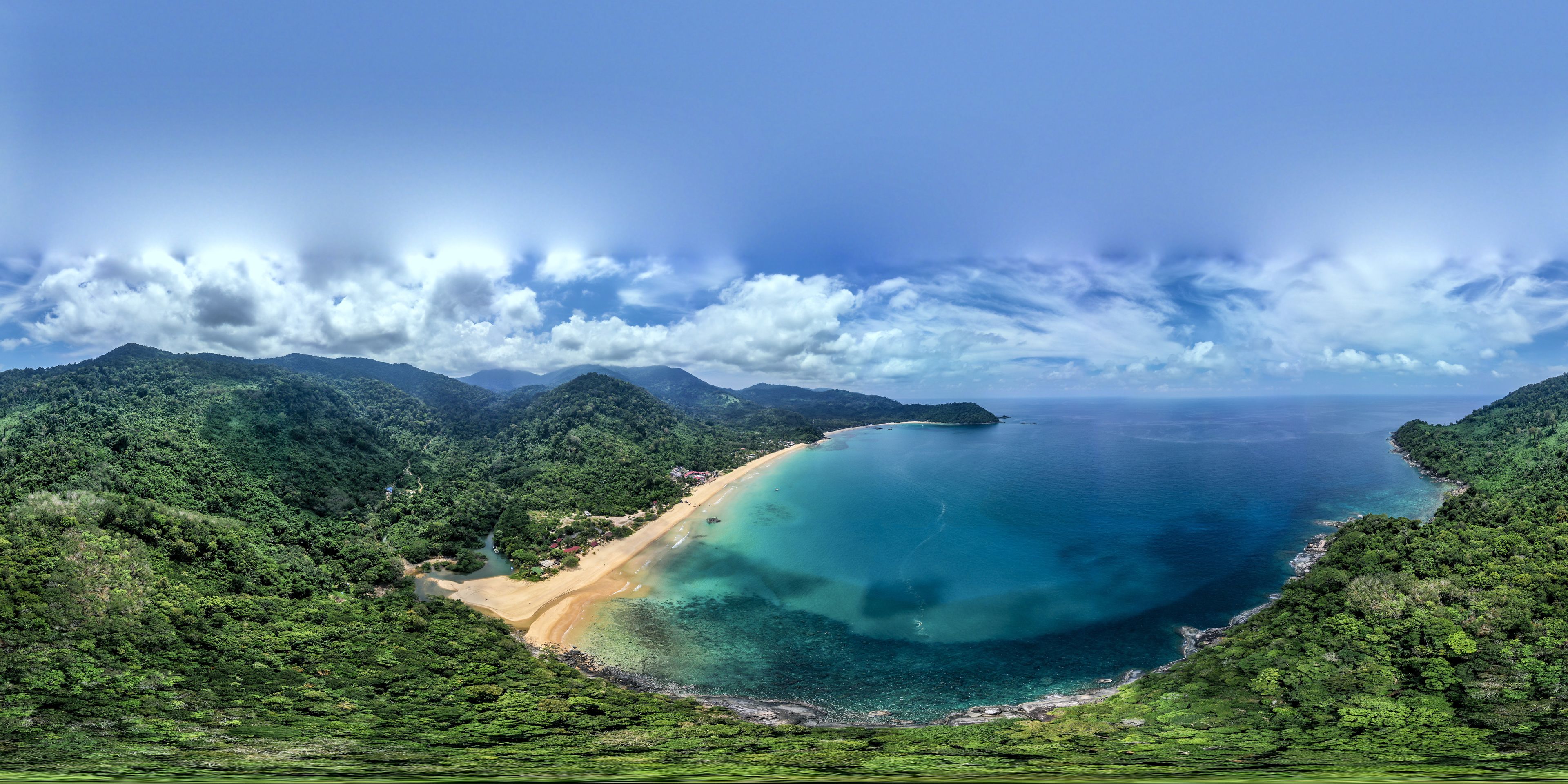 Eine Küstenlandschaft mit Strand, bewaldeten Hügeln und blauem Himmel.
