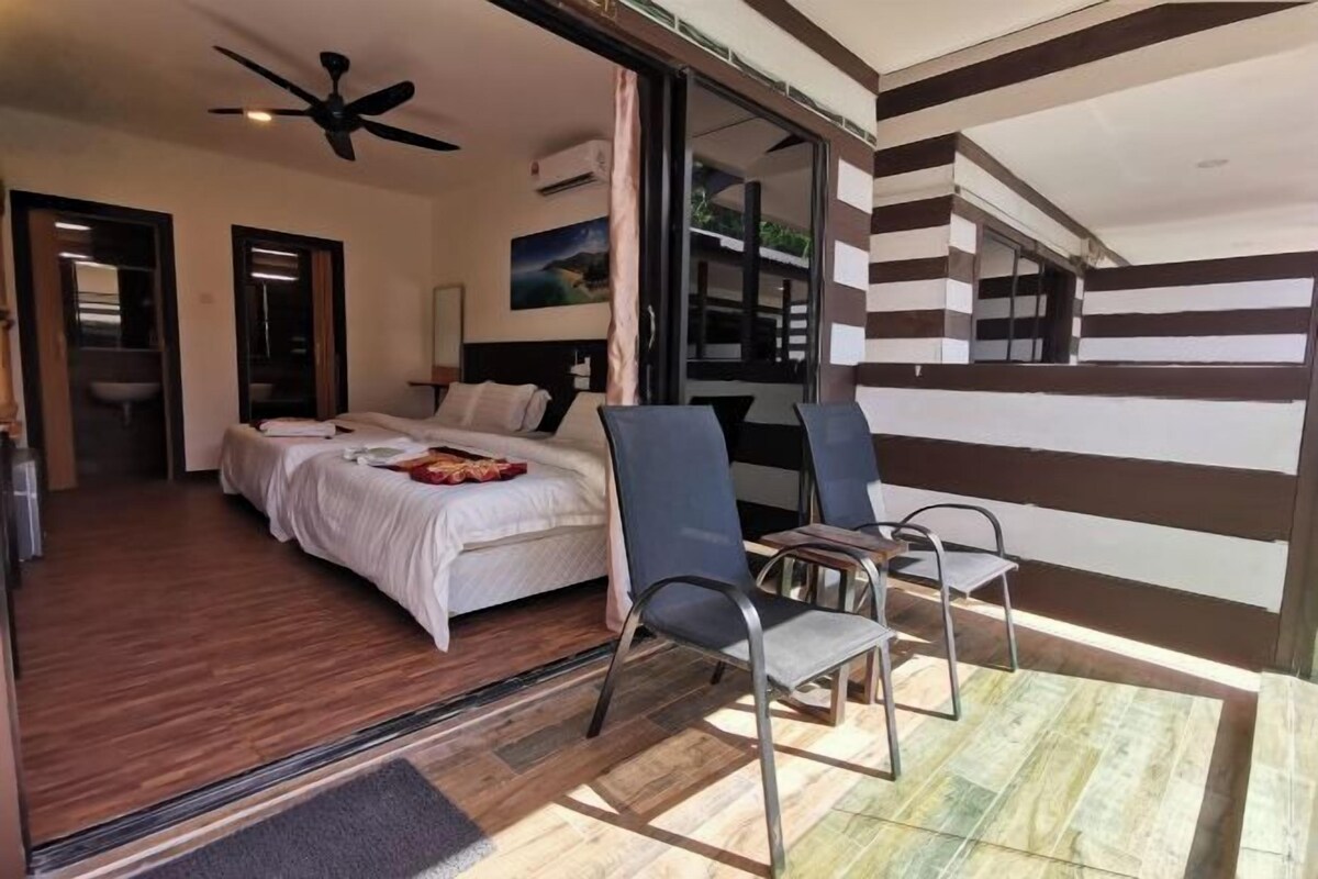 Een hotelkamer met een bed, twee stoelen, een plafondventilator en uitzicht door een glazen deur.