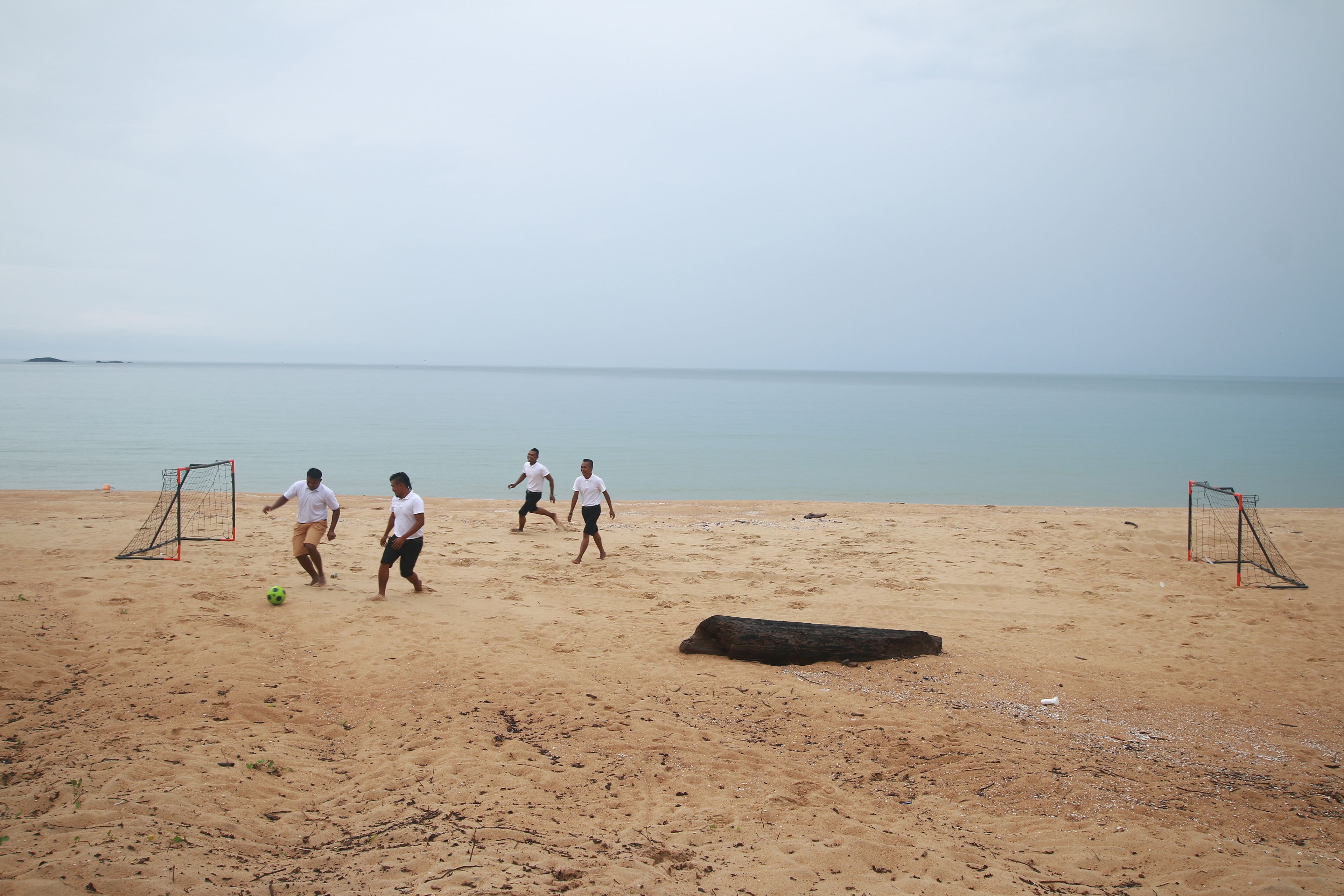 A sandy beach with two soccer goals and a ball.