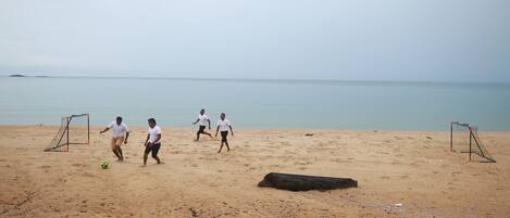 A sandy beach with two soccer goals and a ball.
