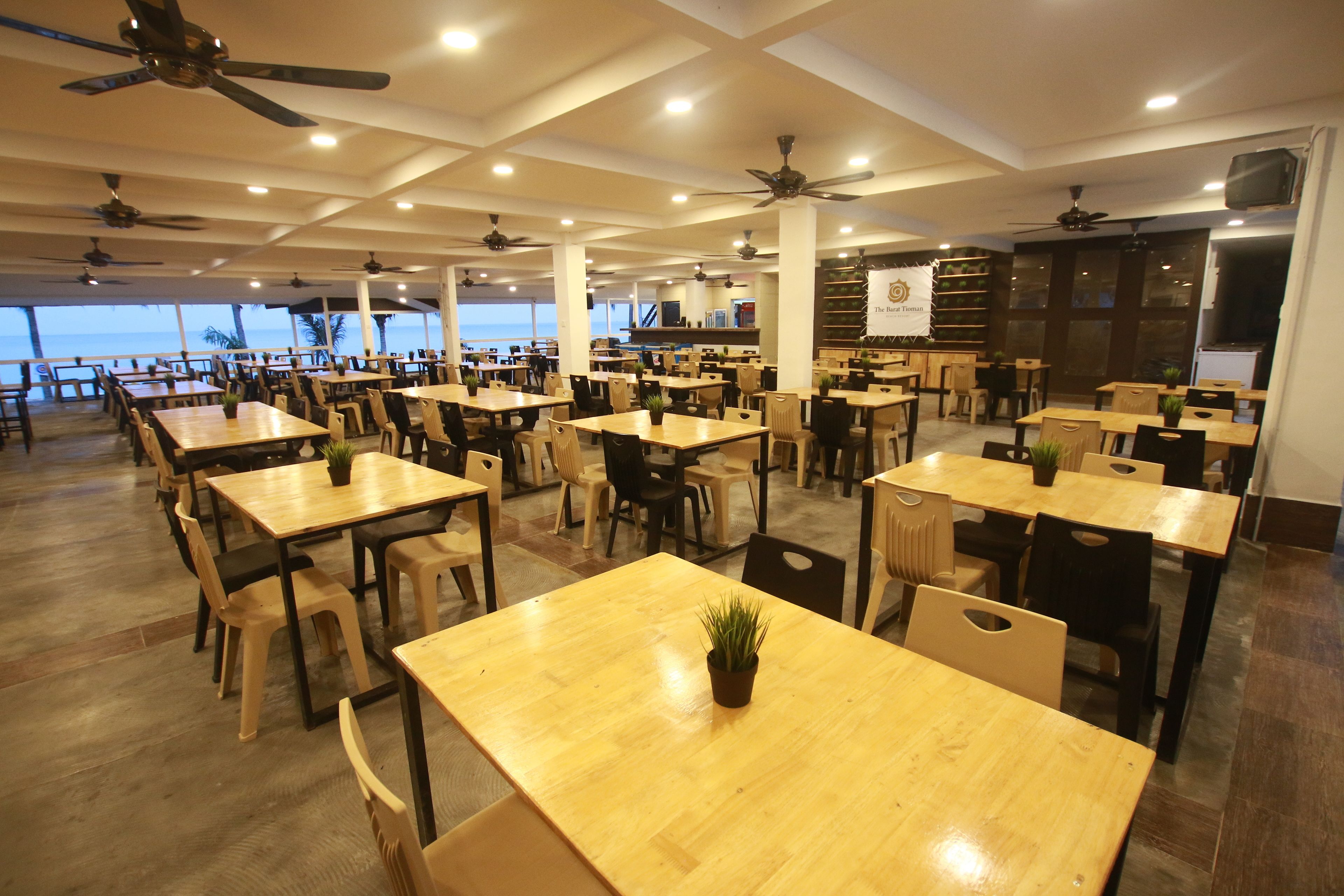 Un restaurante espacioso con varias mesas y sillas, ventiladores de techo y vistas al océano.