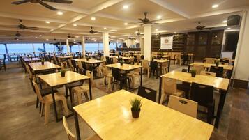 Un restaurante espacioso con varias mesas y sillas, ventiladores de techo y vistas al océano.