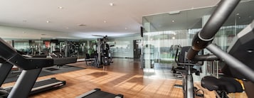 Academia moderna com diversos equipamentos de exercício, piso de madeira e paredes de vidro.