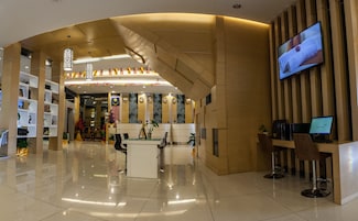 Um hall de hotel moderno com balcão de recepção, computadores e uma grande tela de televisão.