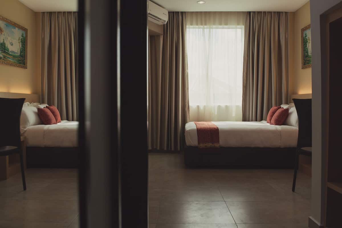 A hotel room with two beds, beige curtains, and a large window.