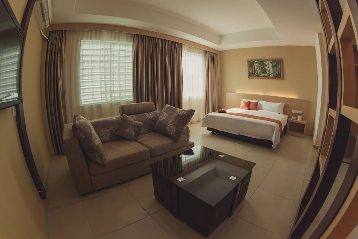 A hotel room with a sofa, a bed, a coffee table, and a painting on the wall.