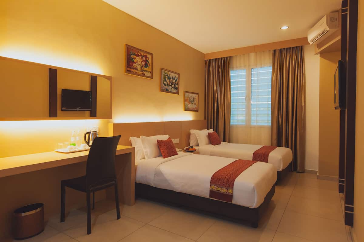 A hotel room with two beds, a desk, a chair, and a window with curtains.